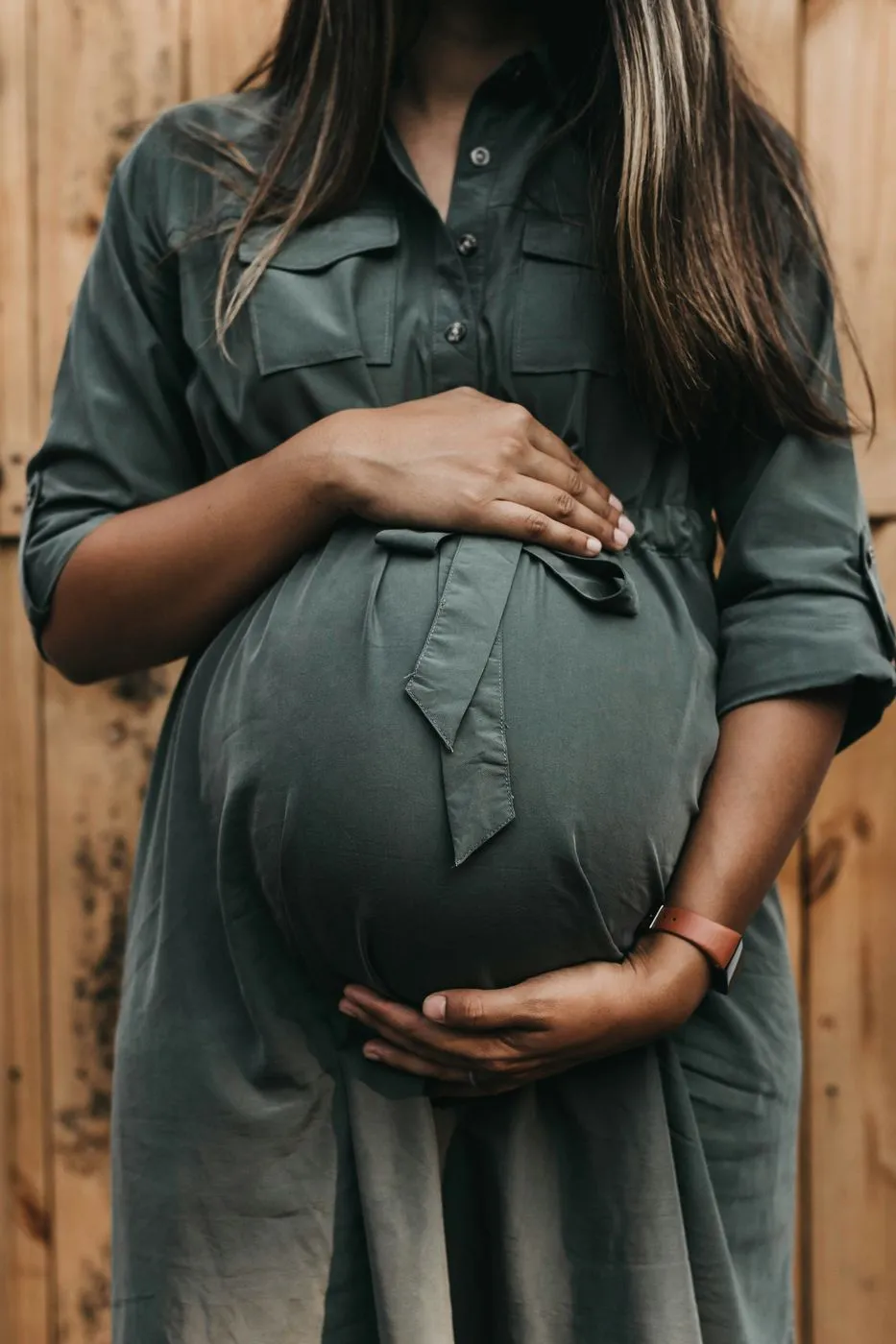 Femme enceinte en robe verte devant une porte en bois, les mains autour de son ventre