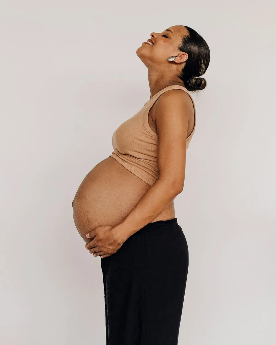 Femme enceinte de profil, souriante, la tête levée et les mains sous son ventre