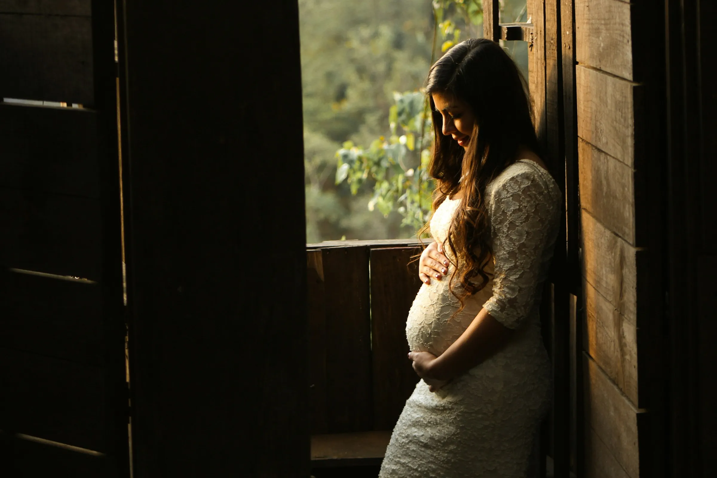Femme enceinte près d’une fenêtre, lumière dorée