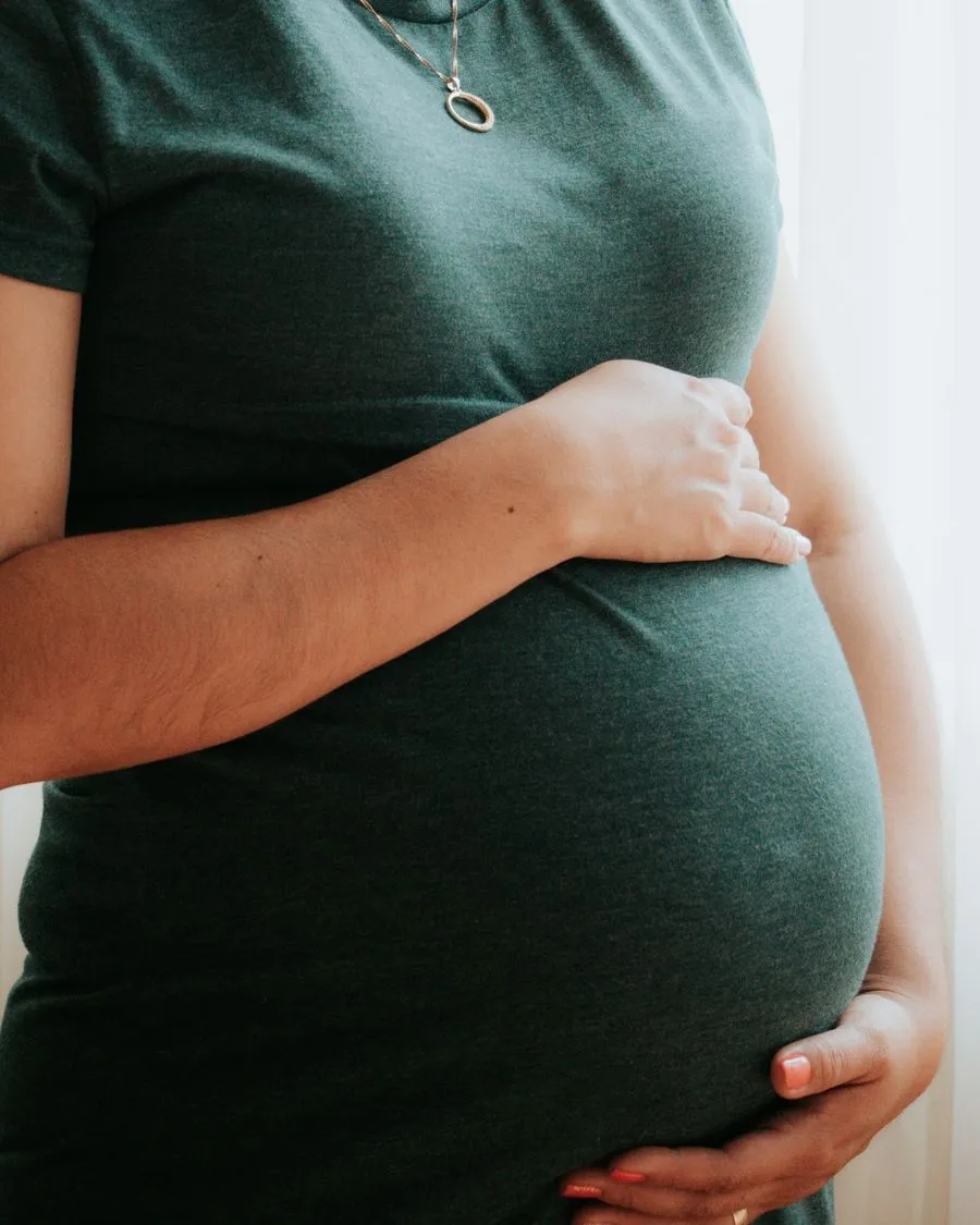 Femme enceinte en t-shirt vert, les deux mains posées autour de son ventre