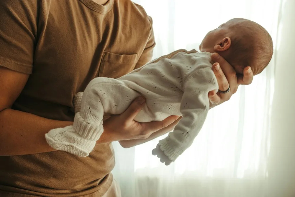 Père tenant son nouveau-né près d’une fenêtre