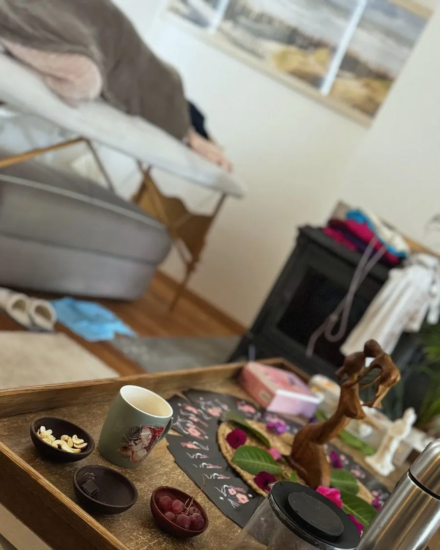 Femme au repos sous une couverture sur la table de soin, plateau de tisane, fruits et cartes d’oracle au premier plan